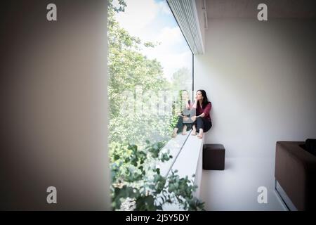Jeune femme attentionnés assise à la fenêtre avec vue sur les arbres Banque D'Images