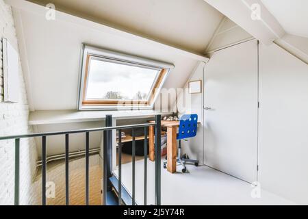 Chaise bleue sur une petite table en bois placée près de la fenêtre dans un grenier clair avec porte blanche fermée et méta clôture à la maison Banque D'Images