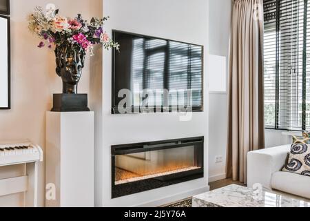 Mur avec TV moderne et cheminée avec cheminée près du bouquet de fleurs dans la chambre lumineuse et élégante avec rideau à la fenêtre Banque D'Images