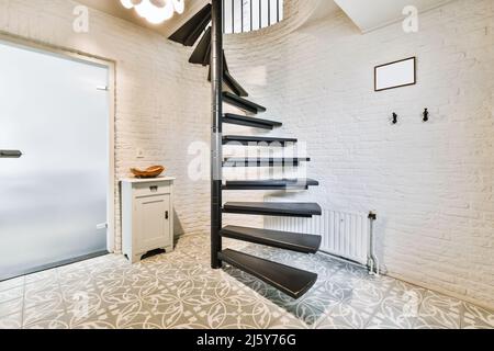 Escalier en colimaçon de couleur noire placé au mur de briques blanches dans un couloir spacieux avec portes fermées dans un appartement moderne Banque D'Images