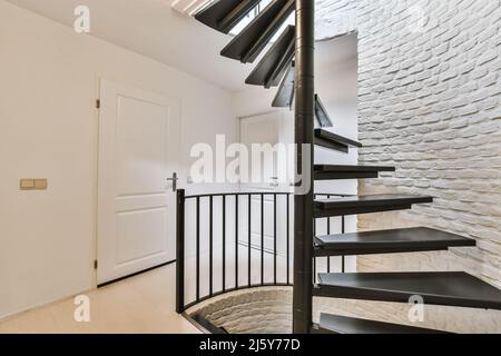 Escalier en colimaçon de couleur noire placé au mur de briques blanches dans un couloir spacieux avec portes fermées dans un appartement moderne Banque D'Images