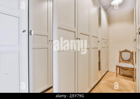 Intérieur de la chambre lumineuse avec grande armoire avec portes blanches et miroir et chaise de style classique Banque D'Images