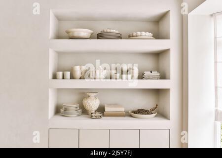 Elégant plateau en céramique tasses et vases disposés sur des étagères intégrées dans un appartement de style minimaliste avec parquet en bois à la lumière du jour Banque D'Images