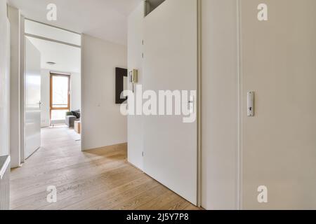 Couloir élégant avec murs blancs menant à la porte ouverte de la pièce avec fenêtre et canapé confortable dans spacieux appartement lumineux conçu dans un minimum de vent Banque D'Images