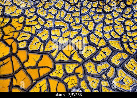 Fond abstrait plein cadre de terre texturée avec sol sec et diverses fissures bleues créant des motifs sur la surface jaune Banque D'Images