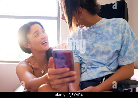 Mère heureuse et fille handicapée en fauteuil roulant avec smartphone Banque D'Images