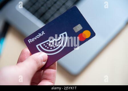 Main humaine tenant une carte de débit Revolut. Paiement numérique de l'application de téléphone mobile en ligne avec un ordinateur portable Banque D'Images