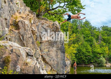 BRNO, République Tchèque - août 2 2020 : homme sautant d'une falaise dans l'eau. Saut dangereux dans l'eau. Saut à l'eau du rocher. Eau peu profonde Banque D'Images