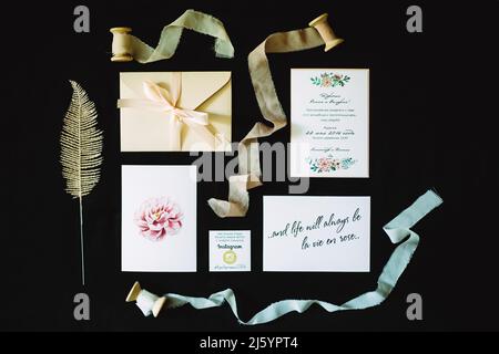 Ensemble de décorations de mariage : calligraphie, cartes d'invitation, enveloppe, dentelle et rubans sur fond noir. Pose à plat, gros plan. Concept de mariage rustique. Banque D'Images