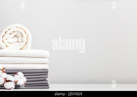 Une pile de draps gris et blancs, des draps et un rouleau de serviettes sur une table avec une branche de coton. Banque D'Images