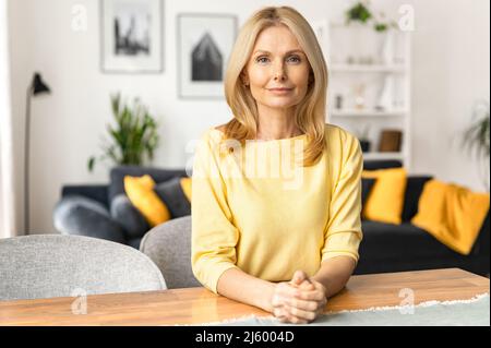 Charmante femme de race blanche regardant la caméra et sourires, se reposer, sereine femme passant un week-end à la maison. Portrait en gros plan sur une femme aux cheveux blonds à l'intérieur de la maison Banque D'Images