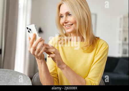 Bonne femme mûre parlant en ligne sur un téléphone mobile via une connexion vidéo, participant à une conférence, assis à la table vidéoconférence à la famille ou à des collègues Banque D'Images