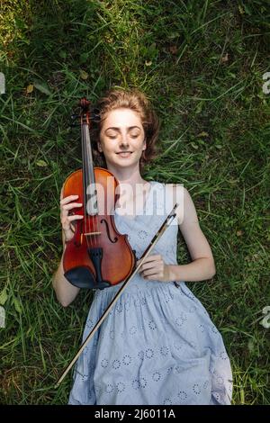 La jeune fille est avec un violon sur l'herbe dans un parc de la ville. Banque D'Images