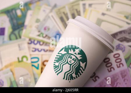 KHARKIV, UKRAINE - 16 DÉCEMBRE 2021 : gobelet en papier blanc avec logo Starbucks et billets d'argent. Starbucks est le plus grand café du monde avec plus de 20 000, Banque D'Images