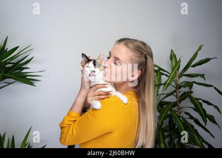 jeune femme blonde portant son chat l'embrassant sur la tête. le chat n'aime pas et colle la langue. Banque D'Images