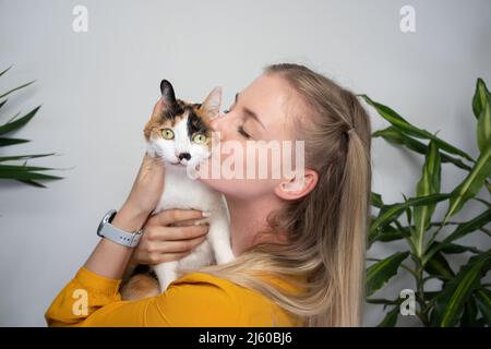 jeune femme portant son calico chat embrassant et embrassant le chaton qui est mécontent à ce sujet Banque D'Images