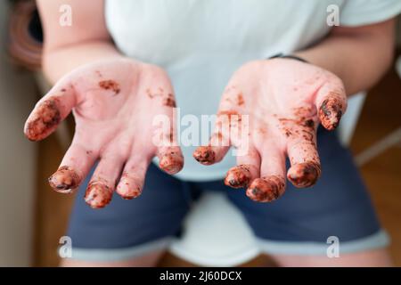 L'homme montre ses mains, tous les doigts couverts de chocolat fondu. Amusement, anniversaire, vacances, fête Banque D'Images