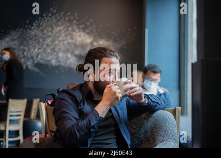 Cheveux longs hispanique jeune adulte homme boire dans une tasse au café hippster Banque D'Images