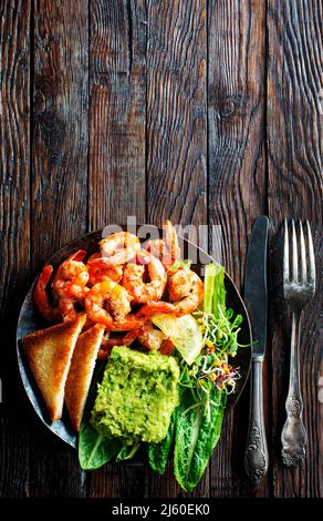 Hors-d'œuvre ou en-cas de crevettes bruschetta à l'avocat. Crevettes frites et purée d'avocat sur une assiette noire Banque D'Images