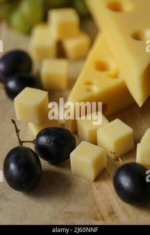 Triangles au fromage Mazdar, cubes de fromage gouda et raisins noirs et verts. Fromage aux raisins, baies sur fond de bois. Banque D'Images