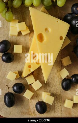 Fromage coupé avec des fruits.triangles de fromage Mazdar, cubes de fromage gouda et raisins noirs et verts.fromage aux raisins baies sur fond de bois. Et Banque D'Images