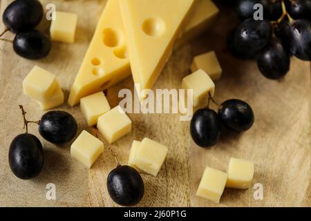 Fromage coupé avec des fruits.triangles de fromage Mazdar, cubes de fromage gouda et raisins noirs.fromage aux raisins baies sur fond de bois. Produits laitiers. Banque D'Images