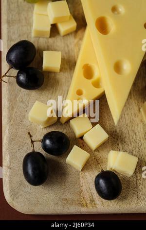 Fromage coupé avec des fruits.triangles de fromage Mazdar, cubes de fromage gouda et raisins noirs.fromage aux raisins baies sur bois background.milk de graisse Banque D'Images