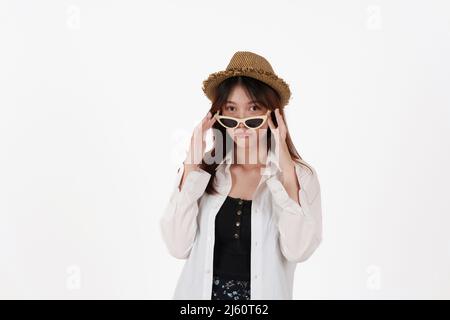 Image d'une jeune femme heureuse portant des lunettes de soleil et un chapeau isolé sur fond blanc. Concept de voyage. Banque D'Images