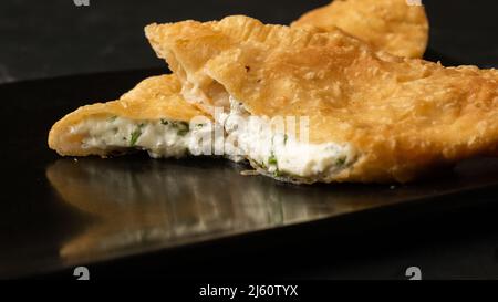 Cuisine orientale ouzbek tatar, chebureau au fromage suluguni un tableau noir. Chebureau - tarte frite. Plat traditionnel turc et mongol Banque D'Images