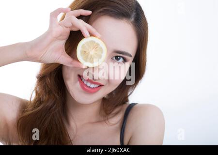 Jolie jeune dame a couvert ses yeux avec une tranche de citron, sur fond blanc - photo de stock Banque D'Images