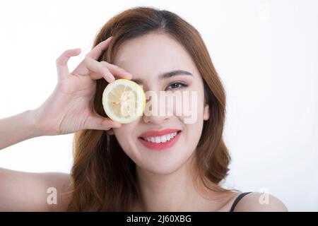 Jolie jeune dame a couvert ses yeux avec une tranche de citron, sur fond blanc - photo de stock Banque D'Images