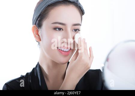 Une jeune femme se regardant dans le miroir utilise une poudre pour appliquer un maquillage professionnel, sur fond blanc - photo de stock Banque D'Images