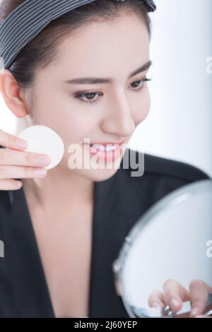 Jeune beauté en face d'un miroir de maquillage est l'application de poudre, sur fond blanc - photo de stock Banque D'Images