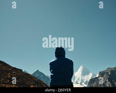 Vue arrière d'une femme asiatique assise au-dessus d'une montagne voisine qui donne sur le mont Yangmaiyong (ou Jampayang en tibétain) à Yading, dans le comté de Daocheng, dans le Sichua Banque D'Images