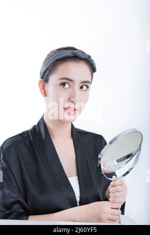 Une élégante jeune et belle dame chinoise se regarde dans le miroir, sur fond blanc - photo de stock Banque D'Images
