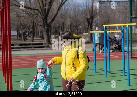 Maman marche avec sa fille tenant les mains. Une fille avec de longues queues de porc. Femme dans une veste jaune avec des cheveux bruns amples. Mère et fille se promenant Banque D'Images