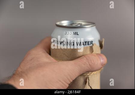 Un homme tient un pot d'eau potable propre dans sa main sur un fond gris. De l'eau fraîche dans la CAN. Aide humanitaire aux Ukrainiens dans le besoin d Banque D'Images