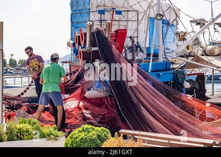 Île d'Aegina, Grèce - 04.27.2022: Pêcheurs tirant et tapissant des filets de pêche au port de l'île d'Aegina. Petite entreprise industrielle locale grecque Banque D'Images