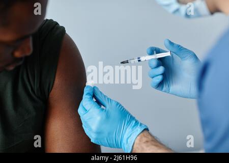 Jeune militaire noir fort vacciné contre le coronavirus dans l'épaule par un médecin dans un masque de protection et des gants Banque D'Images