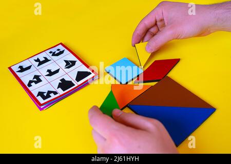 Homme à la main jouant au tangram et faisant la maison, le concept de jeu d'enfants, les formes colorées isolées sur fond jaune, jouant au puzzle tangram jouet, l'apprentissage par p Banque D'Images