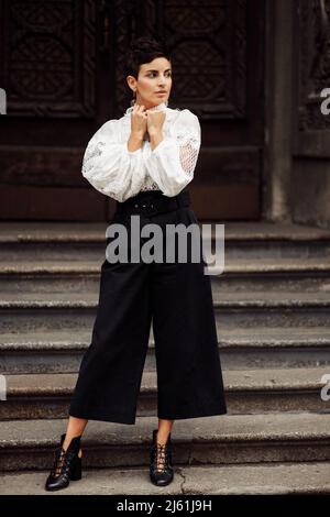 Femme tendance et attrayante regarde l'appareil photo, pose dans un vêtement classique. Belle et élégante promenade de femme d'affaires dans la rue. Réussi en toute confiance Banque D'Images