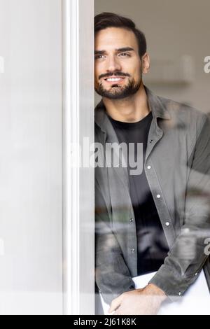 Homme souriant s'inclinant sur la porte vu à travers le verre Banque D'Images