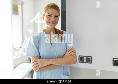Dentiste souriant debout avec les bras croisés dans la clinique dentaire Banque D'Images
