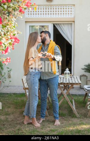 Couple embrassant et montrant le signe du coeur avec les mains dans le jardin arrière Banque D'Images