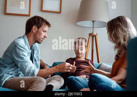 Les parents jouent au titre de ciseaux de papier de roche avec leur fils assis sur un canapé à la maison Banque D'Images