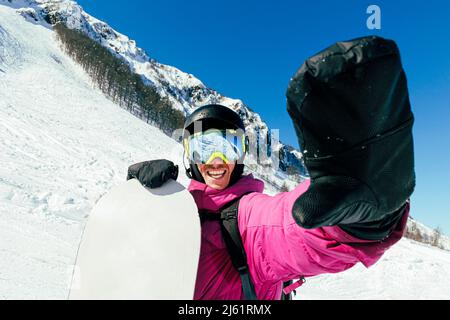 Homme heureux tenant un snowboard debout dans une montagne enneigée Banque D'Images