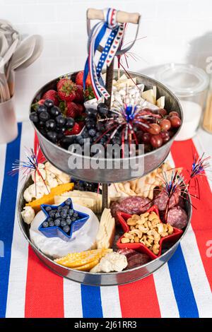 Le 4 juillet, un plateau de charcuterie est servi sur un support métallique à deux niveaux rempli de fromage, de craquelins, de salami et de fruits frais Banque D'Images