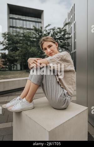 Jeune femme assise en face d'un bâtiment moderne Banque D'Images