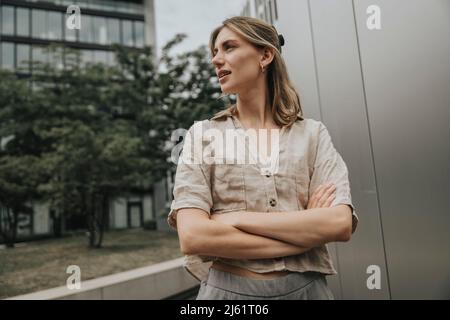 Jeune femme debout avec les armes croisées devant le bâtiment moderne Banque D'Images