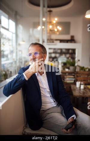 Homme d'affaires attentionné avec main sur le menton assis au café Banque D'Images